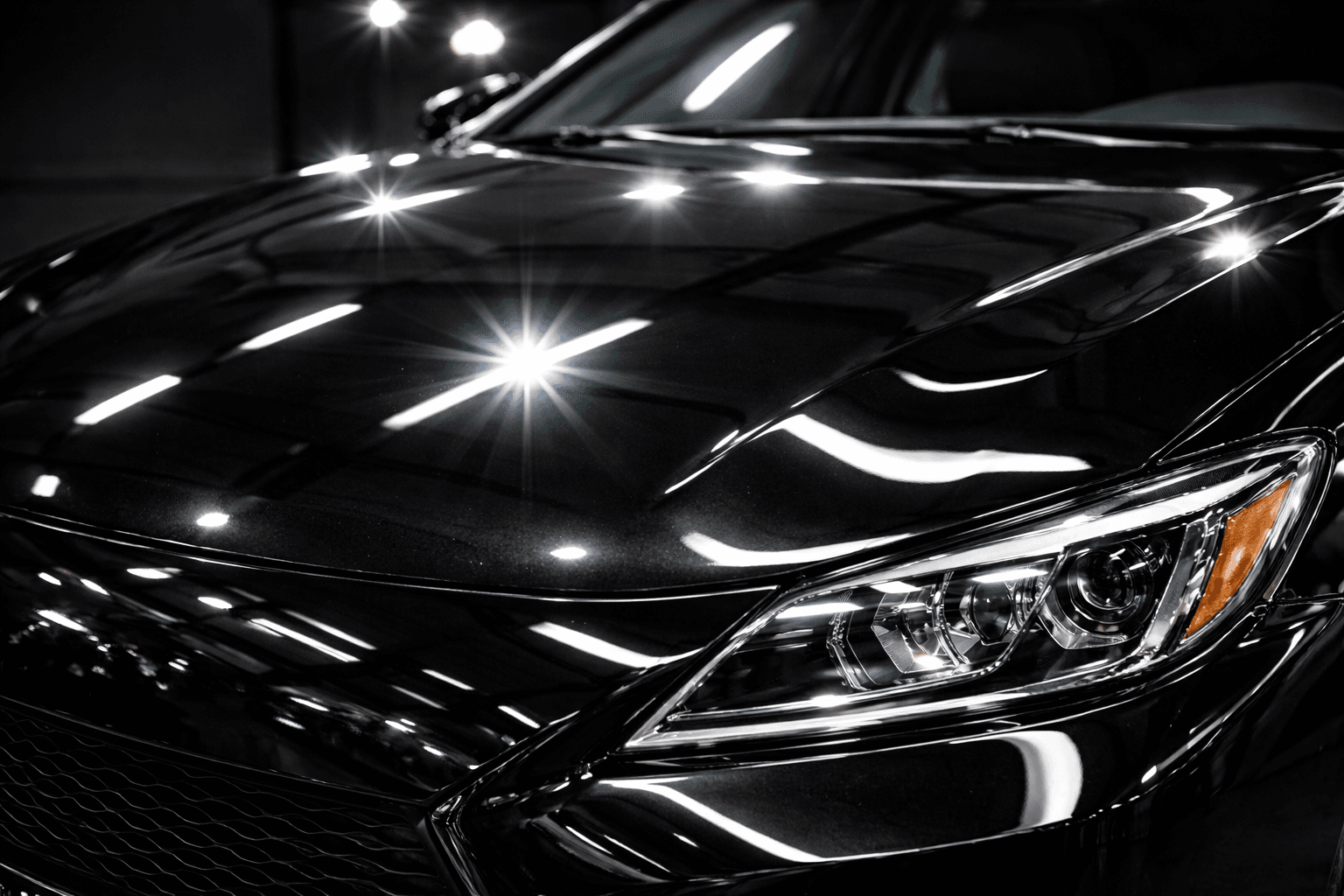 Close-up of a glossy black car reflecting overhead lights with mirror-like clarity.
