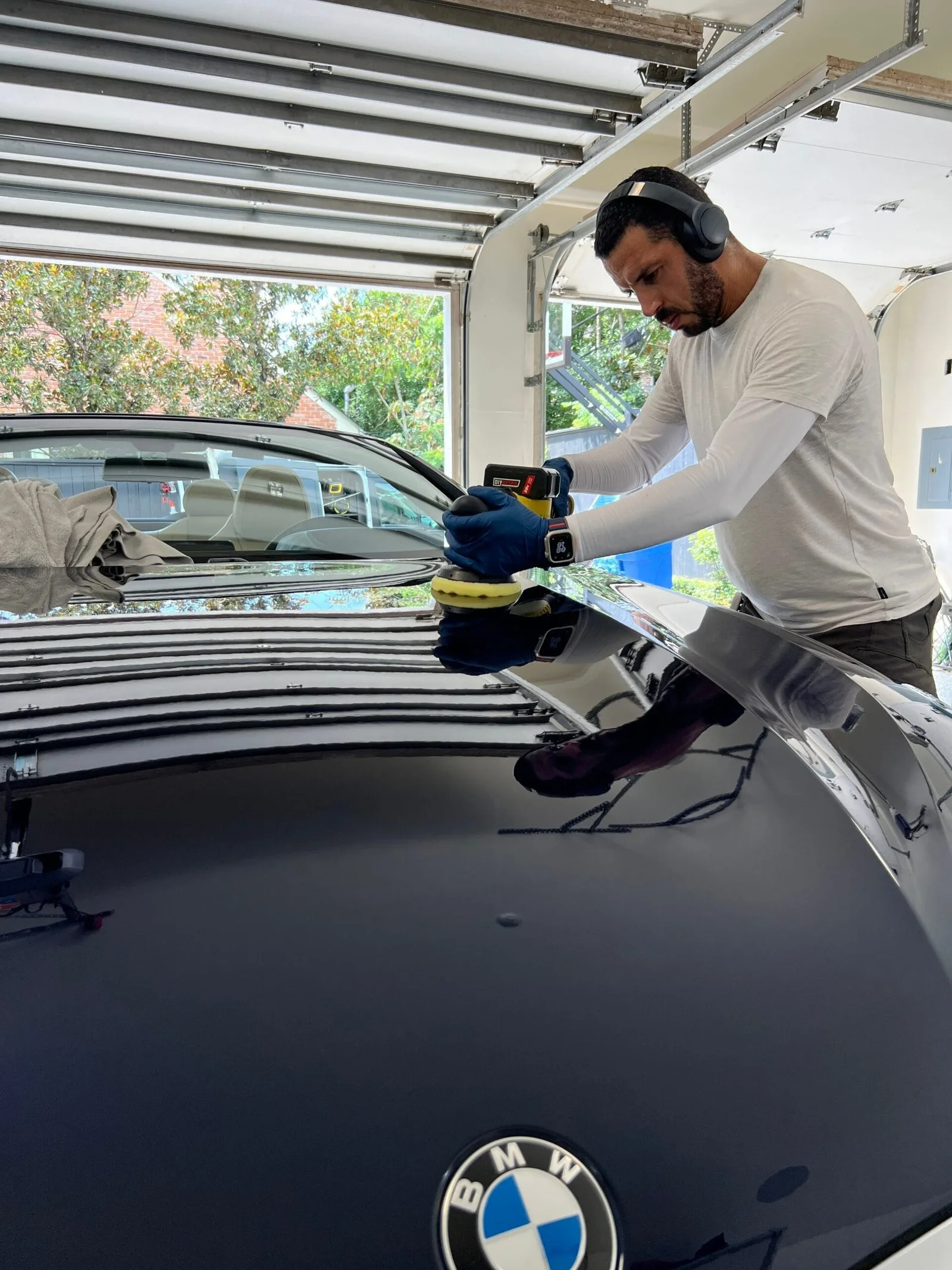 Azul detailer machine-polishing the hood of a black BMW in a home garage
