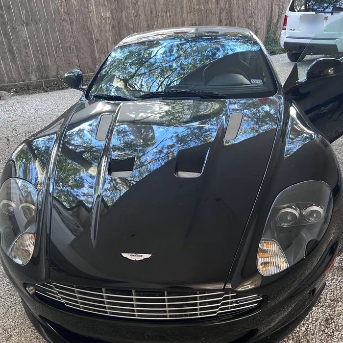 Black Aston Martin DBS after a detail, its hood reflecting the trees