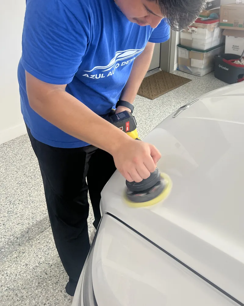An Azul technician machine-polishing a white vehicle in a client garage