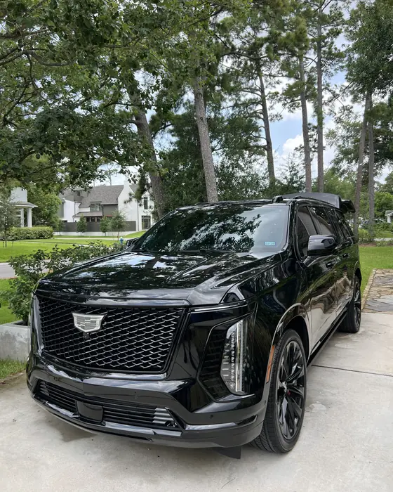 Black Cadillac Escalade after ceramic coating, under tall pine trees