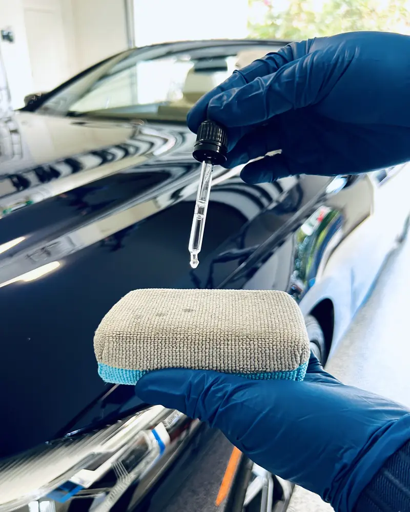 Gloved hand loading ceramic coating onto an applicator beside the polished BMW