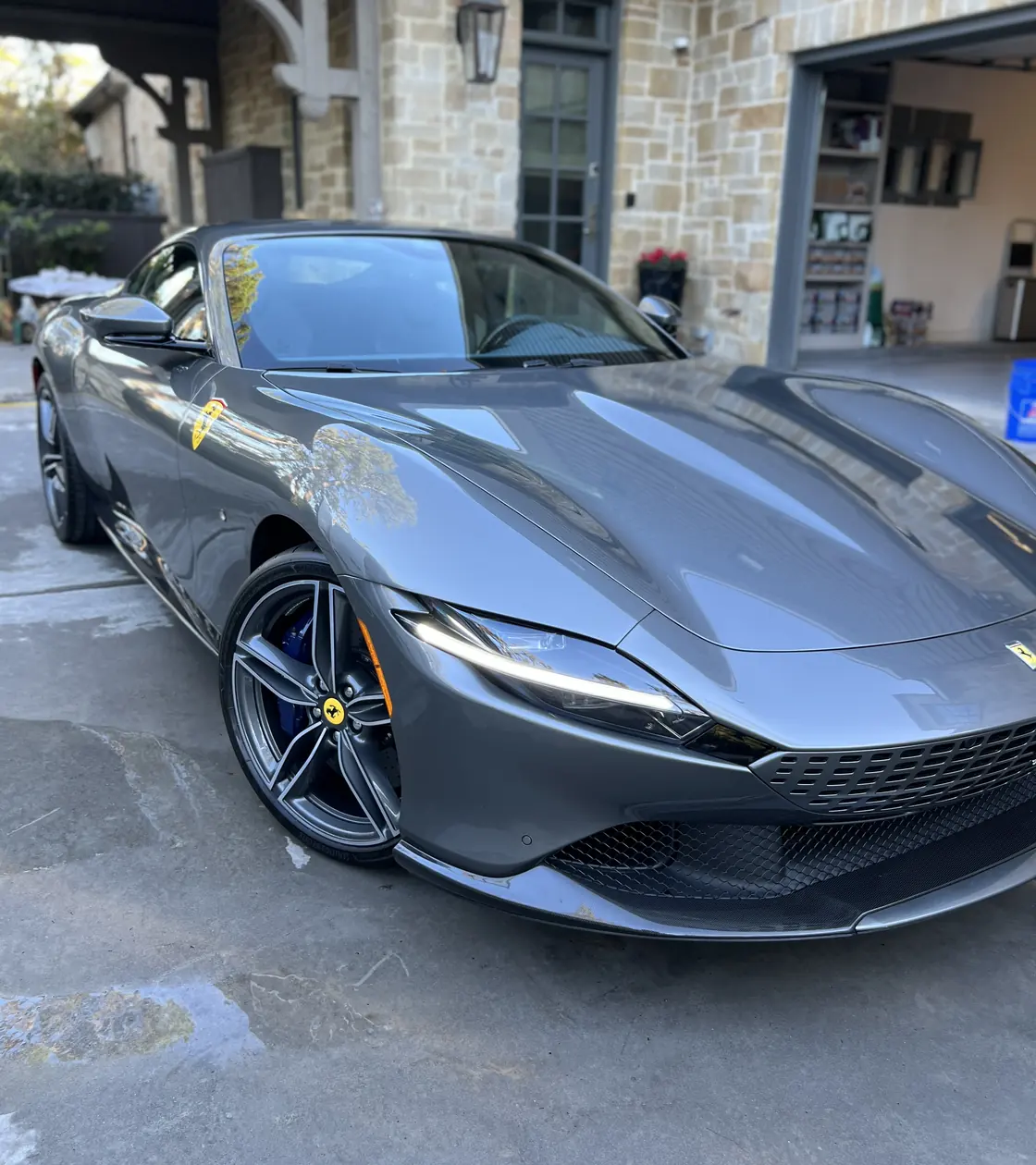 Grey Ferrari Roma after an Azul ceramic coating, with the trees reflected along its front fender, parked outside the client's garage in Houston