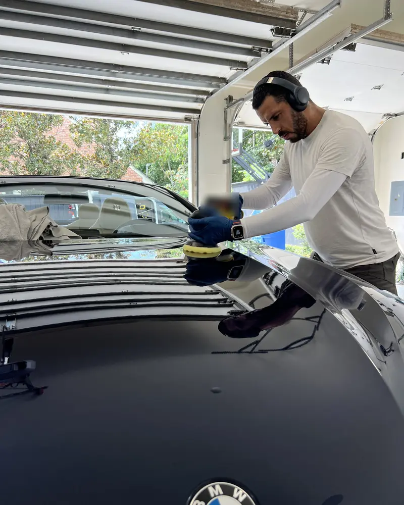 Azul machine-polishing a BMW's hood in the client's garage before ceramic coating