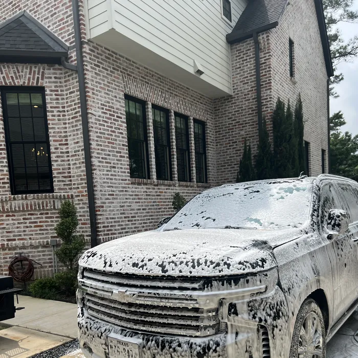 Chevrolet Tahoe covered in wash foam during a hand wash beside a brick home