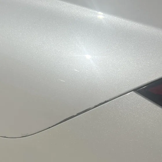 Fine scratches on a pearl-white rear quarter panel, visible only near the reflection of direct sun