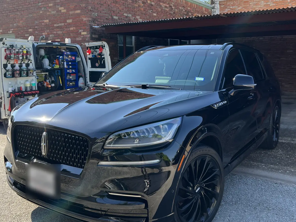 Azul's mobile detailing van, doors open to show its product shelves, beside a black Lincoln Aviator in a client's driveway