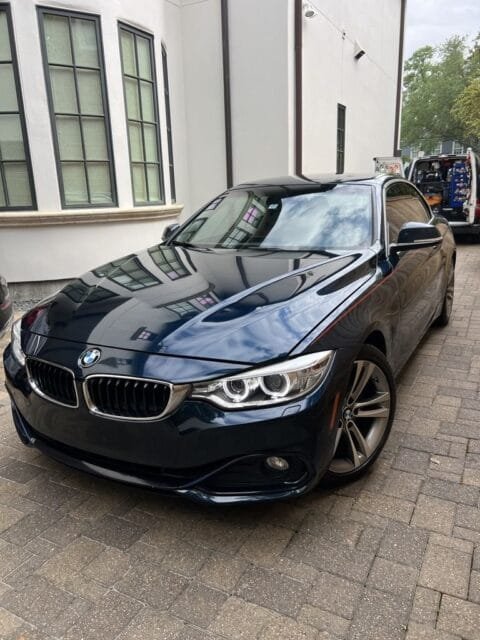 After: the same BMW 4 Series with a clean, glossy hood reflecting the building beside it