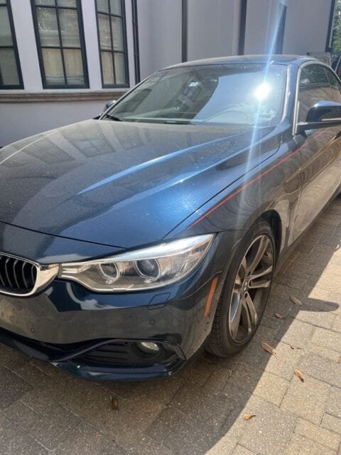 Before: dark blue BMW 4 Series hood and fender with a dull, dusty film, in direct sun