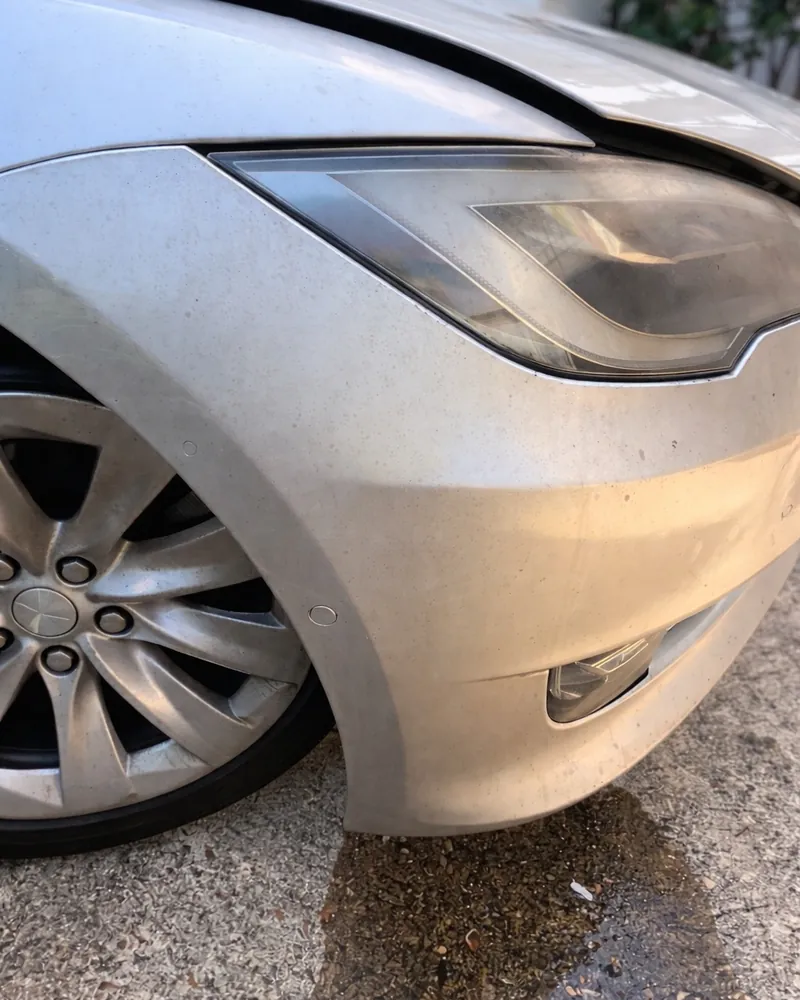 Silver Tesla front fender and bumper under hazy, stained seven-year-old paint protection film, before polishing
