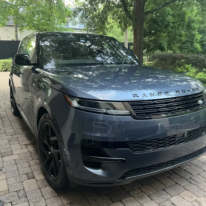 Blue-gray Range Rover Sport after a detail, under trees on a paver driveway