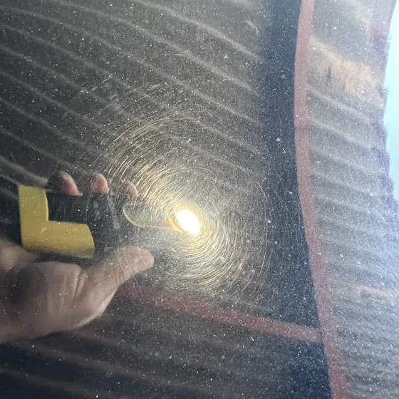 Circular swirl marks on black paint lit by a flashlight