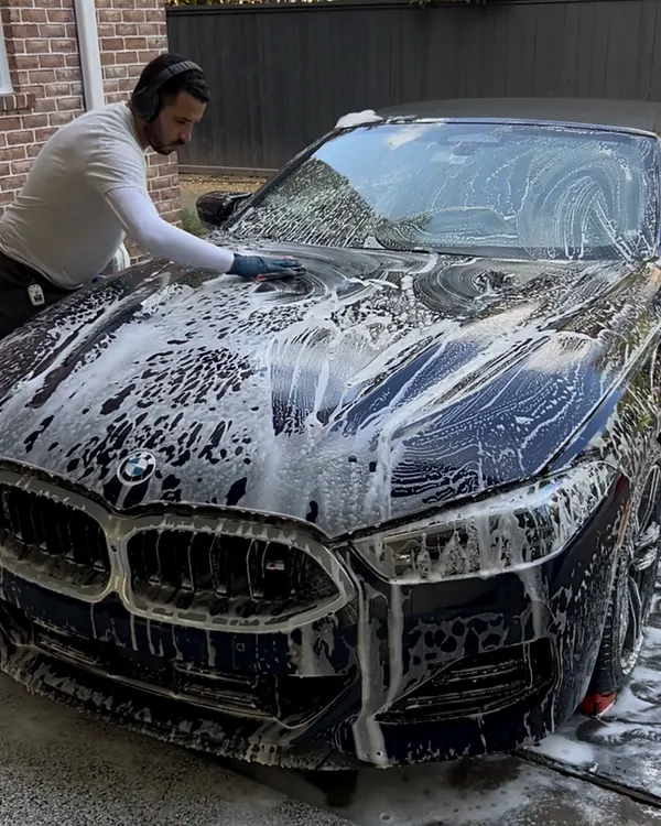 Nassim hand washing a black BMW 8 Series convertible on a Houston driveway