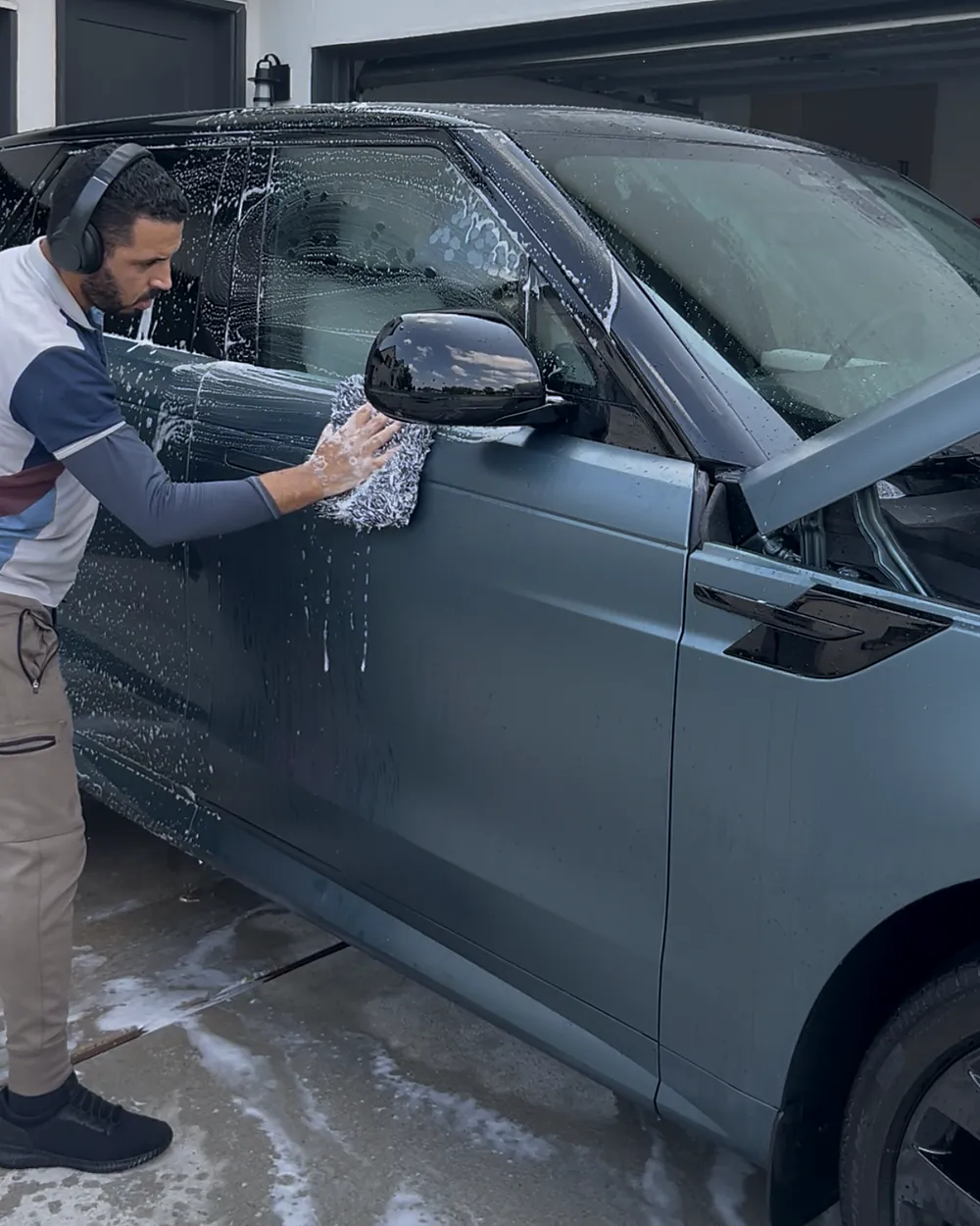 Nassim hand washing a matte teal Range Rover in a Houston driveway with a microfiber wash mitt