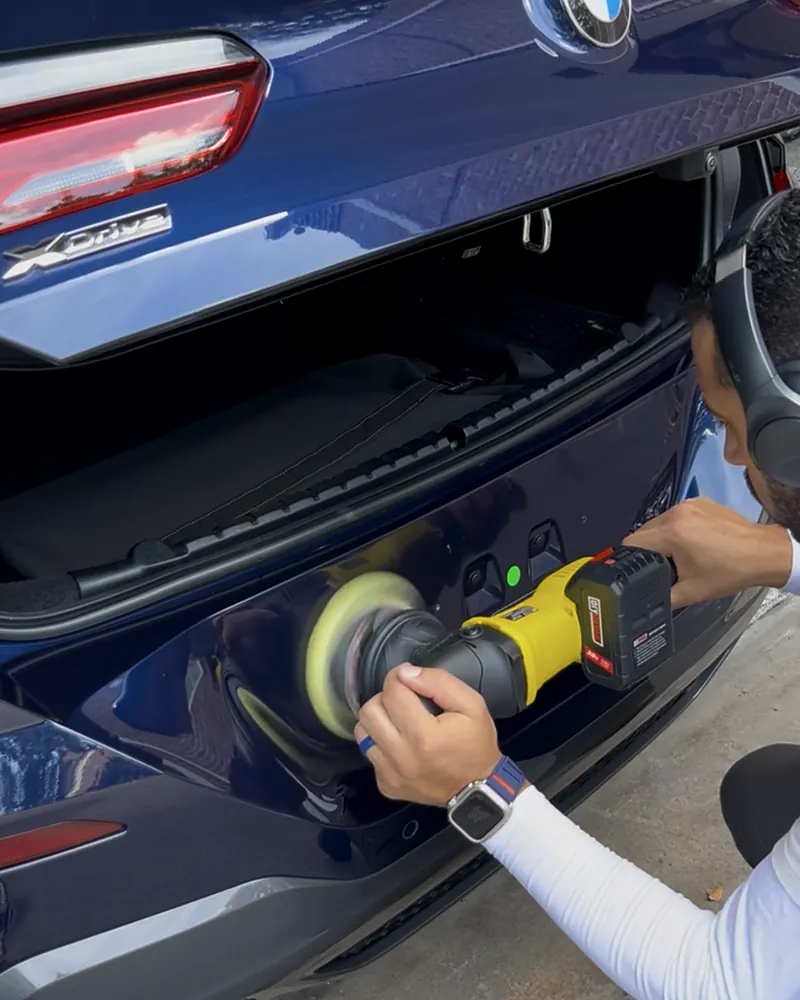 Nassim machine polishing the rear of a blue BMW X5 during a mobile detail in Houston