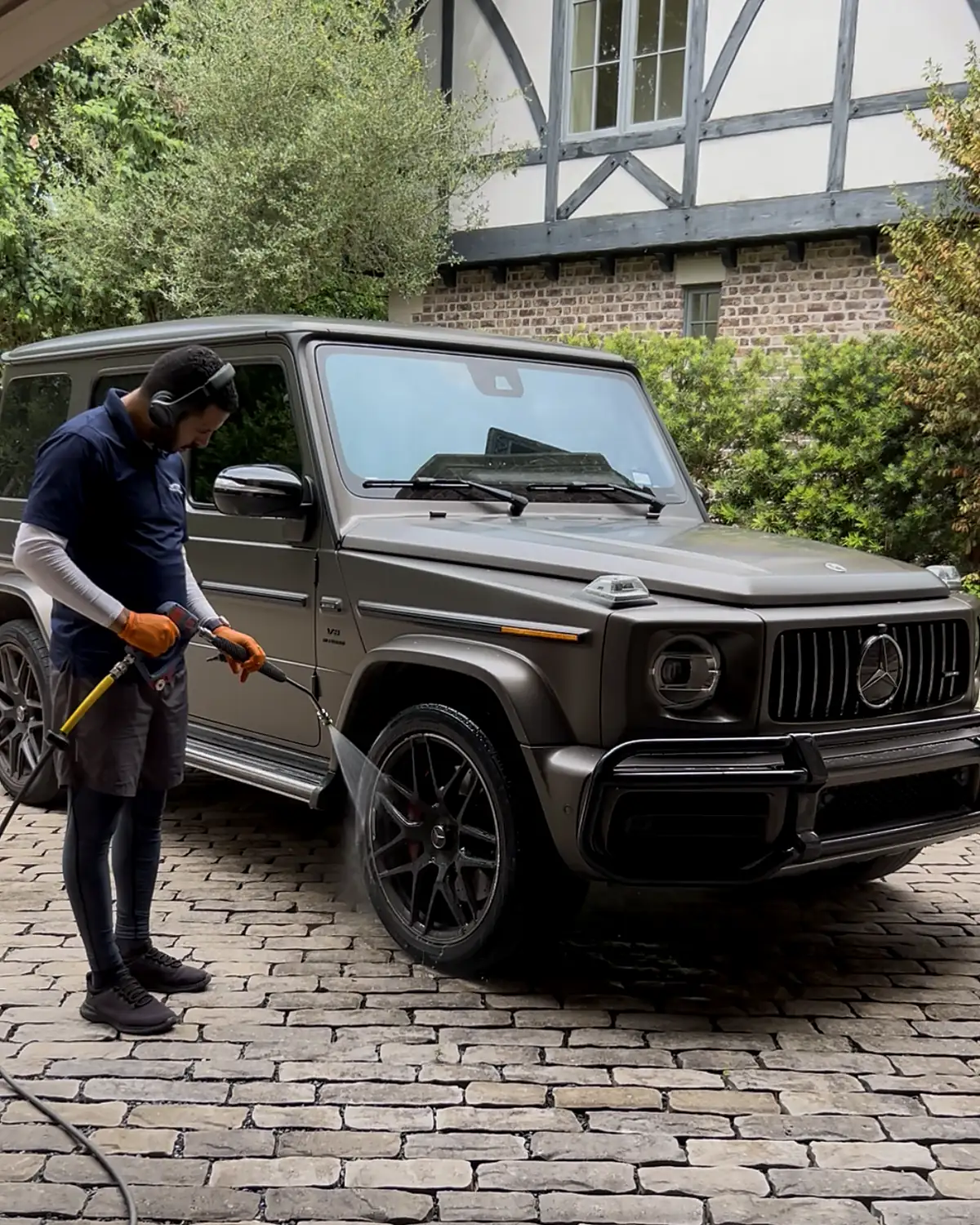 Nassim, founder of Azul Auto Detailing, rinsing a matte gray G-Wagon on a client's driveway in Houston