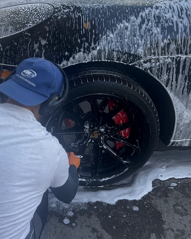 Nassim of Azul Auto Detailing, in an Azul cap, cleaning a Porsche wheel with red brake calipers